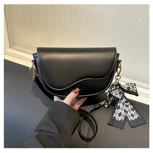 Detail view of black matte leather saddle bag featuring gold clasp and plaid silk scarf