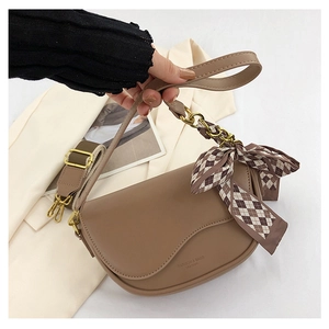 Close-up of brown leather saddle bag featuring a silk scarf metal chain and wide strap