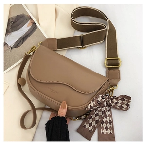 Close-up of tan leather saddle bag with wide fabric strap and silk scarf detail
