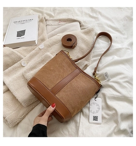 Detail of a brown suede bucket bag featuring contrast leather trim and golden metal buckles