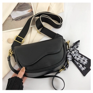 Close-up of black leather saddle bag with wide woven strap and checkered silk scarf