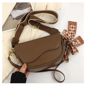 Close-up of brown leather saddle bag featuring a bow scarf and wide woven shoulder strap