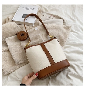 Close-up of beige and brown leather bucket bag with litchi texture and gold metal hooks
