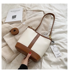 Detail shot of a two-tone bucket bag with cream pebble leather and brown trim on white bedding