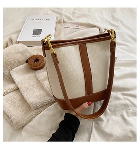 Detail of cream textured bucket bag featuring brown leather trim and golden metal hardware