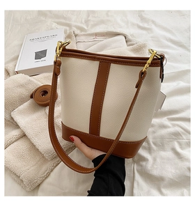 Detail of minimalist cream bucket bag with brown leather trim and golden hardware