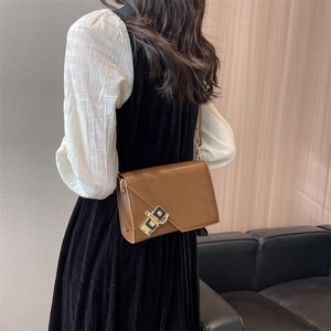 Close-up of brown leather crossbody bag with square metal lock and chain on model
