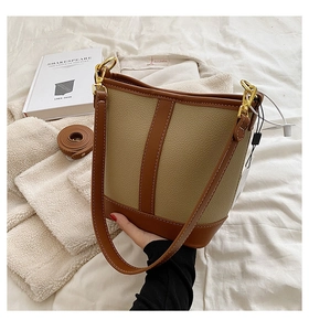 Detail of beige and brown leather bucket bag with contrast stitching and gold metal rings