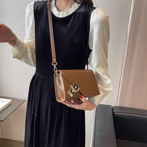 Detail of brown faux leather crossbody bag with gold buckle on model black dress