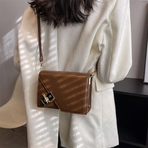 Close-up of brown leather crossbody bag with asymmetric flap and vintage metal lock detail