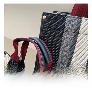 Detail of woven tote bag showing striped fabric, red handle, and gold metal lock
