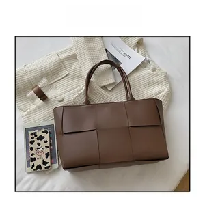 Detailed view of brown woven leather tote bag on bed with modern lifestyle props