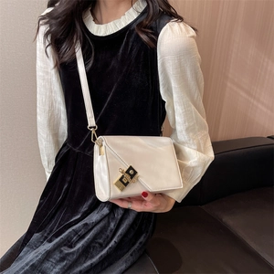 Detail of minimalist cream square crossbody bag with gold hardware and chain on a dress