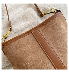 Close-up of brown suede shoulder bag with gold metal hook and white contrast stitching