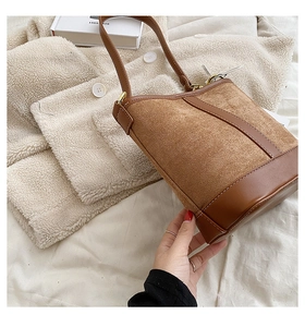 Detail of a brown bucket bag with suede texture and leather trim on white fabric