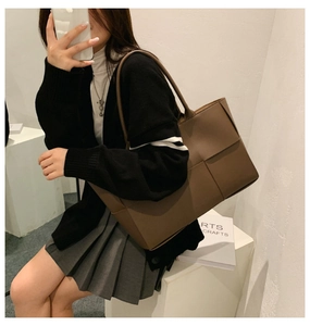 Deep brown minimalist woven tote bag shown on a model in a minimalist indoor setting