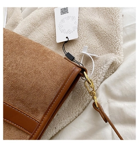 Detailed close-up of brown suede bucket bag with white stitching and gold metal hardware