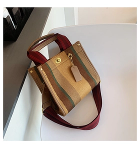 Detail of canvas stripe tote with leather trim, metal turn-lock and woven shoulder strap