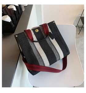 Detailed side view of a striped canvas tote bag with red straps on a white chair