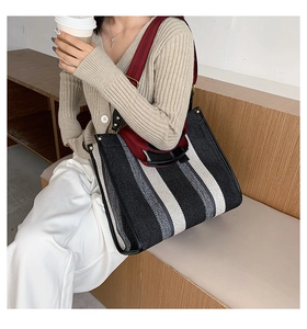 Close-up of a striped tote bag featuring knit texture, leather handles, and a long shoulder strap