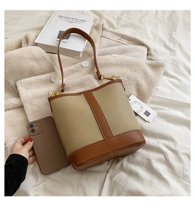 Detail of a beige and brown paneled bucket bag with lychee grain texture and gold hardware