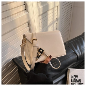 Detail of a minimalist cream crossbody bag with gold hardware and leather strap