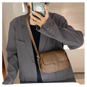 Detailaufnahme der braunen Satteltasche mit Litschi-Muster getragen über einem Blazer