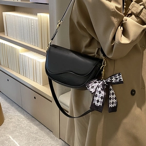Fashionable black leather saddle bag with a bow charm and golden hardware detail