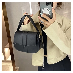 Detail einer matt-schwarzen Satteltasche aus Leder mit Goldschnalle und Schulterriemen