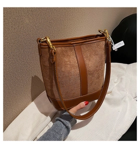 Detail of a brown bucket bag showing contrast stitching, matte texture and golden hardware