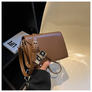 Detail of dark brown leather crossbody bag with golden chain and clasp in a lifestyle setting