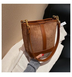 Detail of a brown suede bucket bag with leather stitching and gold metal hooks
