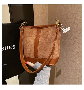 Close-up of brown suede bucket bag featuring smooth leather panels and gold hardware