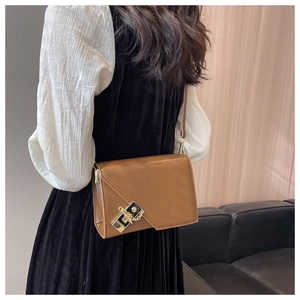 Detail view of a caramel leather crossbody bag with modern asymmetric flap and gold buckle
