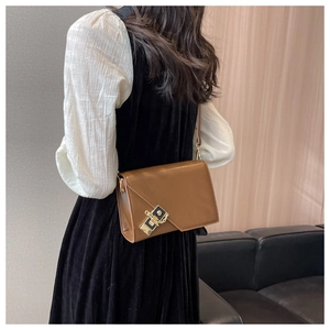 Detail view of brown faux leather shoulder bag with golden lock on white shirt outfit