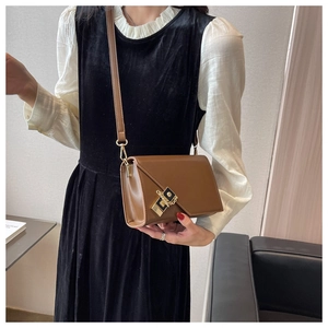 Brown crossbody bag with unique asymmetric flap and gold-tone metal lock shown on model