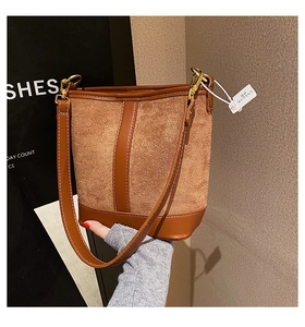 Detail of brown contrast stitching bucket bag with suede panels and gold hardware buckle