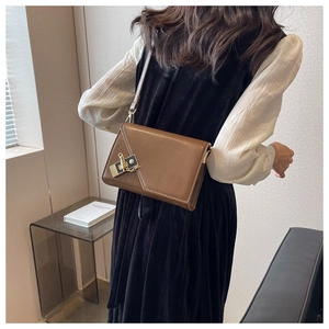 Detail of a brown leather crossbody bag featuring a unique geometric flap and metal chain