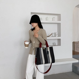 Minimalist striped tote bag with red handles and shoulder strap shown in a bright interior