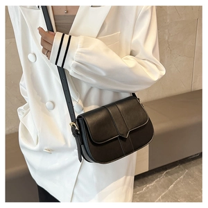 Detail einer minimalistischen schwarzen Satteltasche aus glattem Leder am weißen Blazer