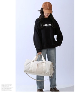 Off-white gym bag shown by model with woven handles and adjustable shoulder strap