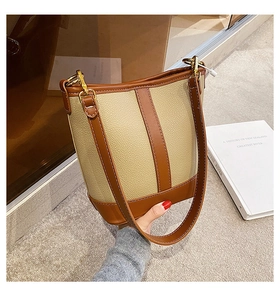 Detail of minimalist bucket bag featuring beige lychee texture and brown leather stitching