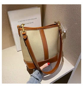 Detail of a brown leather and beige grained bucket bag displayed on a wooden shelf