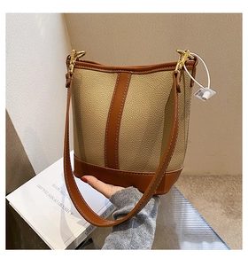 Close-up of contrast stitching on a khaki and brown leather bucket bag with gold hardware