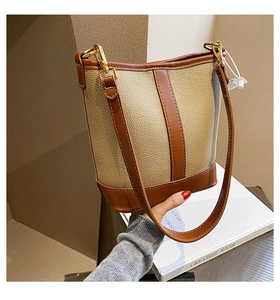 Detail of beige lychee textured bucket bag with brown leather trim and gold hardware