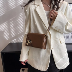 Brown rectangular crossbody bag in smooth leather with gold buckle on white blazer