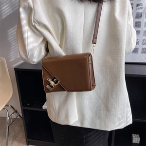 Brown faux leather crossbody bag with gold metal buckle and chain on white blazer
