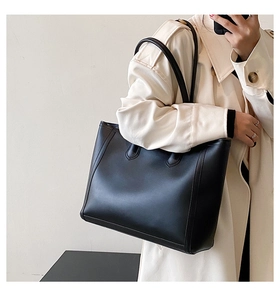 Detail of minimalist black leather tote bag showing side stitching on a long trench coat