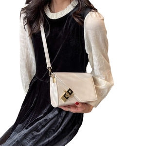 Chic cream-colored crossbody bag with asymmetric flap and metal buckle on black dress