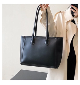 Detail of minimalist black tote bag with vertical stitching and slim straps on beige coat